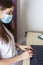 Young woman in medical mask working for laptop, portable computer from home on light background. Distance learning and work online