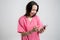 Young woman medical professional nurse or doctor dressed with pink hospital clothes holding smartphone, texting, looking nervously