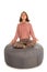 Young woman meditates while sitting in the lotus position on round shape grey beanbag chair