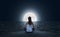 Young woman meditating on the beach at full moon