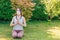 Young woman meditating outdoors in a park or garden with surgical facemask