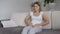 Young woman with menstrual pain sitting on sofa and holding hands on stomach