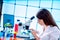 Young woman with microscope in GMO laboratory. Study of green plant of agricultural plants with a microscope