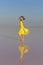 A young woman in the middle of a pink salt lake stands in a bright yellow dress and meets the sunset.