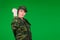 Young woman in military uniform shows her fist to the camera on a green background with blank space. Strong fearless