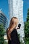 Young woman with mobile phone on modern downtown high-rises skyscrapers street city view background. Confident girl with