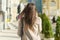 Young woman with mobile phone walking in the sunny city street, girl wearing warm coat, view from the back, golden hour