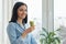 Young woman morning at home near the window drinking freshly blended green kiwi fruit smoothie in glass, vitamin drink in winter