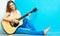 Young woman musician with guitar sitting on a floo