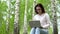 Young woman in nature with a laptop in her hands. A girl sits on a stump in a birch forest and leads works through a