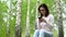 Young woman in nature with a phone in her hands. A girl sits on a stump in a birch forest and leads works through a