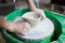 Young woman novice student in the first lesson in pottery tries to make a product from white clay on a potter`s wheel. reportage.