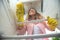 Young woman observed from the inside of a refrigerator doing some shelf cleaning