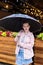 Young woman in open pink raincoat standing waiting patiently under an umbrella