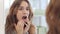 Young woman with opened mouth checking teeth in mirror in home bath room