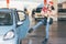 Young woman opening door of her car with leg foot while her hands are full of christmas gifts and presents boxes