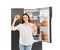 Young woman with oranges near open refrigerator on white background