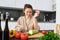 Young woman orders groceries on mobile app. Girl in bathrobe sits in the kitchen with vegetables, looking for recipe to