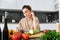 Young woman orders groceries on mobile app. Girl in bathrobe sits in the kitchen with vegetables, looking for recipe to
