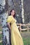 Young woman outddors in historical yellow dress leaning on tree