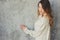 Young woman in oversize knitted sweater posing by the grey wall in modern apartment