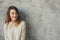 Young woman in oversize knitted sweater posing by the grey wall in modern apartment