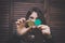 Young woman with painted green clover on her cheek holding golden coin at the bar in front of a wooden wall