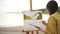 Young woman painter drawing watercolor landscape picture on easel.