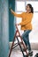 Young woman paints her walls blue using a roller. Painting a wall with paint roller. Interior wall of new house.