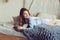 Young woman in pajama wake up in the morning in cozy scandinavian bedroom and lying on bed with oversize knitted blanket