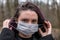 Young woman in park putting on a light, soft protective medical mask for face protection against virus outbreak, close up portrait