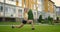 A young woman in the park wearing headphones does yoga. Doing yoga on the grass against the background of houses in the