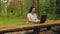 Young woman in a park at a wooden table working with a laptop.