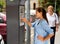 Young woman paying for parking in modern parking meter on city street