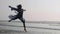 Young woman performing grand jete jump on the beach in slow motion