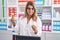 Young woman pharmacist smiling confident holding pills bottles at pharmacy