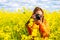 Young woman photographer with a DSLR, wearing an orange jacket, takes a picture in a rapeseed field, rural countryside, Romania