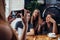 Young woman photographing her positive friends in coffee house using smartphone, background defocused