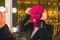 A young woman in a pink balaclava looks in the mirror