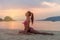 Young woman in pink bra and black panties sitting on beach stretching her legs during sunset at sea. Fitness girl doing