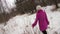 Young woman in pink coat walking in winter forest and touching branches