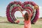 young woman in pink dress and hat stands and rise her hands up on background of flower heart arches love. Image with a
