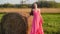 Young woman in a pink dress stands near haystack