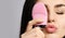 Young woman with pink face exfoliator brush silicone cleansing device for sensitive normal skin relishes incredible softness