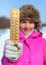 Young woman in pink jacket holds wooden thermometer outside on sunny but cold day, illustrating weather with freezing temperatures