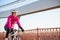 Young Woman in Pink Jacket Riding Road Bicycle on the Bridge Bike Line in the Cold Sunny Autumn Day. Healthy Lifestyle.
