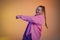 A young woman in a pink shirt poses against an orange studio background. The dancer demonstrates elements of jazz-funk