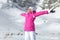 Young woman in pink ski jacket, gloves and pants, arms spread, e