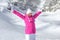 Young woman in pink ski jacket, winter hat and gloves, arms spread above, smiling, looking happy with snow covered mountain