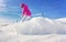 Young woman in pink winter jacket and helmet skiing snow spraying near, clear blue sky above